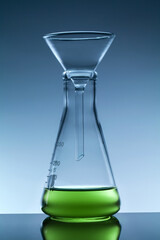 laboratory funnel and conical flask with green liquid on dark blue background.