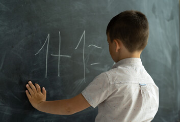schoolboy in the class near the blackboard writes numbers with chalk. Math lesson. Junior School. concept of modern education. Back to school. Place for text.