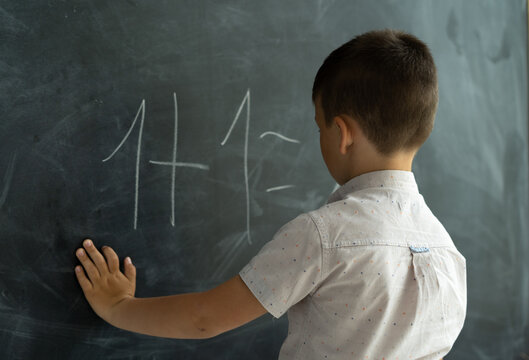 schoolboy in the class near the blackboard writes numbers with chalk. Math lesson. Junior School. concept of modern education. Back to school. Place for text.