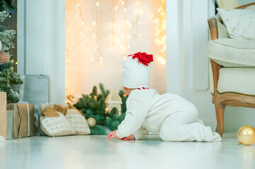 Baby crawls against background of Christmas tree and fireplace in garland. Infancy, babyhood at home at Christmas.
