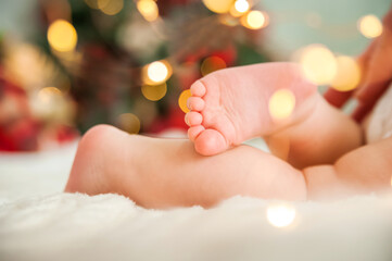 Baby's first Christmas. Feet of newborn close-up on background of New Year's lights and Christmas...