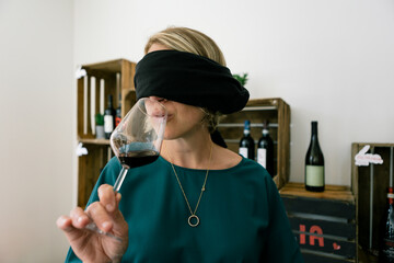 Woman with covered eyes doing wine drink degustation inside bar restaurant - Focus on face wearing blindfold - blind taste concept - obrazy, fototapety, plakaty