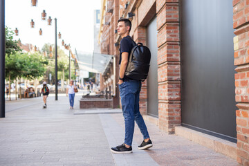 Rear view man walking in city with black leather backpack on his shoulders