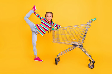 Photo of funky girl hold trolley stretch leg wear striped shirt jeans shoes isolated yellow color...