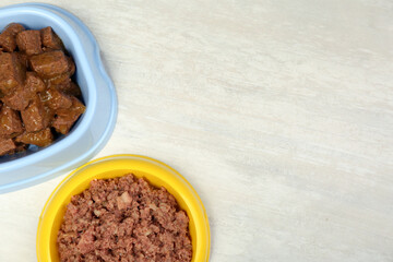 Different pet food in feeding bowls on white table, flat lay. Space for text