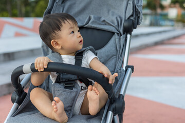portrait image of Happy and cute Asian Chinese baby boy sitting on stroller at park during evening