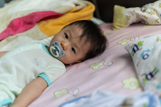Portrait image of cute baby boy with sucking pacifier lying on bed