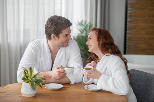 A couple in white bathrobes having coffee and feeling happy