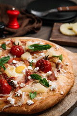 Pita pizza with prosciutto, pineapple, grilled tomatoes and egg on table, closeup