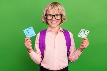 Photo of young happy positive charming boy wear glasses bag bad good grade isolated on green color...