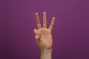 Woman showing three fingers on purple background, closeup