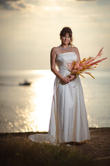 Fototapeta na wymiar Beautiful bride in white wedding dress at sunset near a beach and the ocean or sea coast in United Kingdom