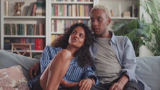 Happy beautiful interracial couple hugging relaxing on sofa in cozy apartment. Smiling millennial African guy embracing pretty Indian girlfriend on couch at home. Young family mortgage loan concept.