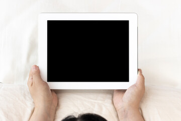 ベッドで寝そべって、タブレット端末を使う若い女性（日本人、30代）