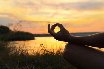 Man meditating near river at sunset, closeup. Space for text