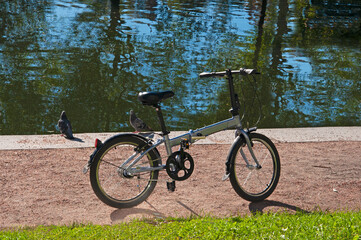 Bicycle and two pigeons on the embankment of the lake with reflection in the city park