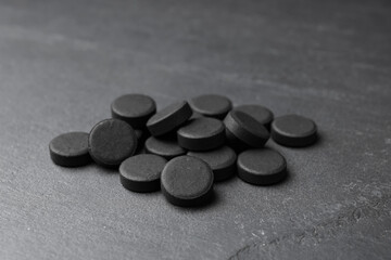 Fototapeta na wymiar Pile of activated charcoal pills on black table. Potent sorbent