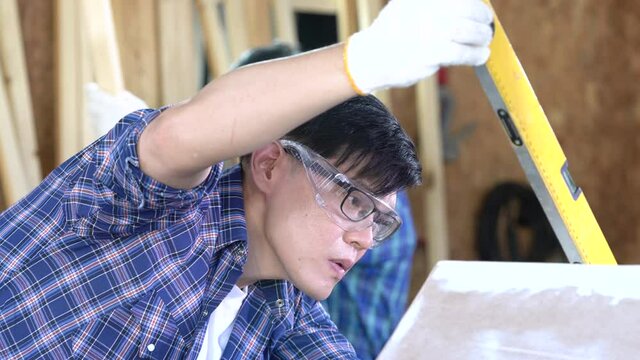 Carpenters are working in a wood factory. Carpenter is using a Water level meter to measure wood sizes. 