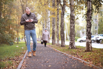 Fototapeta premium Autumn concept. A man walks through the city. Autumn leaves on the footpath.&nbsp;