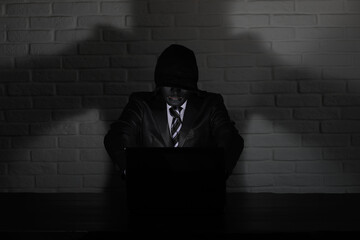 Hacker in black mask and hood at the table
