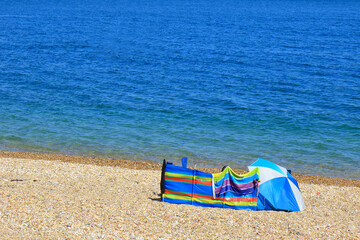 Beach umbrella and wind breaker on a pebbled beach © kevinr4