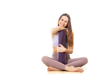 Young sporty female yoga instructor in bright white yoga studio, holding yoga mat, smiling, looking at camera