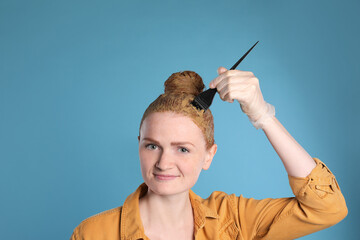 Young woman dyeing her hair with henna on light blue background