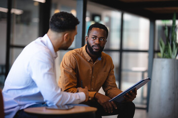 Two diverse male business colleagues using tablet and talking