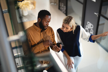 Two diverse male and female business colleagues talking and using smartphone