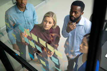 Diverse male and female business colleagues reading colourful memo notes on glass wall
