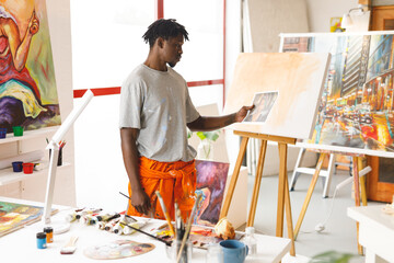 African american male painter at work holding picture in art studio