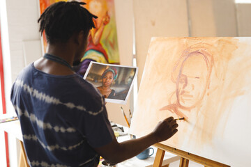 African american male painter at work painting portrait on canvas in art studio - Powered by Adobe