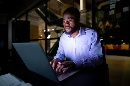 African american businessman working at night, sitting at desk and using laptop