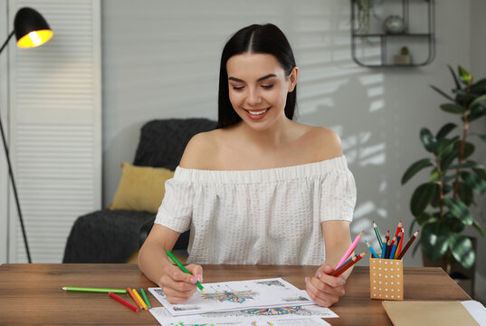 Young woman coloring antistress page at table indoors
