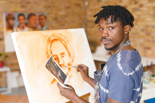 Portrait of african american male painter at work painting portrait on canvas in art studio