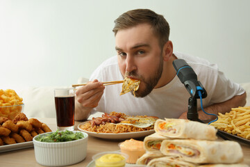 Fototapeta na wymiar Food blogger eating in front of microphone at table against light background. Mukbang vlog