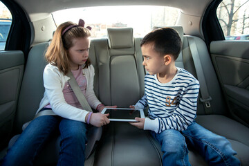 Young brother and sister can’t make a deal about who gets the digital tablet on the backseat of...