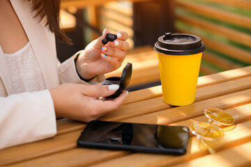 A woman takes out wireless bluetooth headphones from a charging case. A smartphone, sunglasses and...