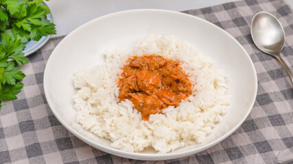 Rice with chicken meat cooked with paprika and sour cream, served with fresh parsley, close up on kitchen table