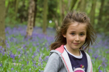 portrait of a pretty little girl with a bluebells forest background in sprintime