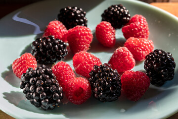 Ripe raspberries and blackberries on a plate of emerald-turquoise color. Topic: raspberry and blackberry dishes, an idea of delicious and healthy food