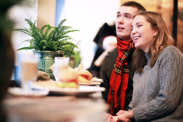Couple in a restaurant or diner eating a hamburger and chicken wings flirting the while, shot with available light, very selective focus