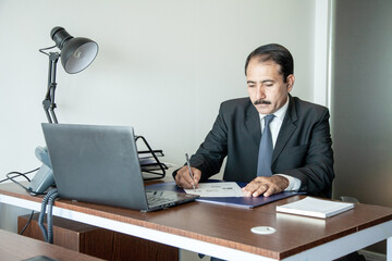 Middle age old business executive with moustache wearing suit and tie writing with pen at his...