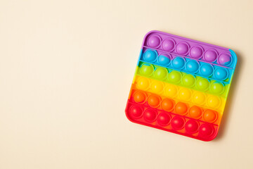 Rainbow silicone sensory antistress pop it toy on light brown background. Top view. Space for text.