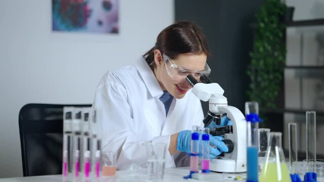 happy woman is viewing virus or bacteria in microscope in laboratory, doing scientific discovery