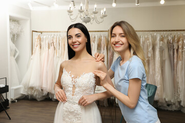 Woman helping bride wear wedding dress in boutique