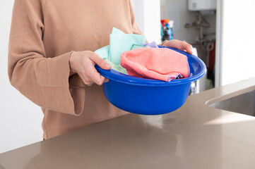 Young woman in the kitchen holding in her hands a basin with cleaning rags.Concept of household...