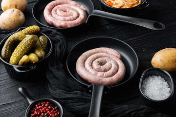Traditional raw spiral pork sausages in cast iron frying pan, on black wooden table background