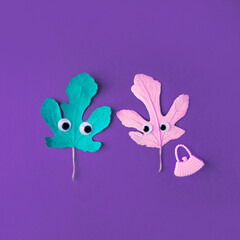 Two autumn leaves in love in pastel colors with eyes and a modern purse. A funny concept of celebrating a minimal holiday. Purple background.