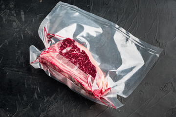 Raw beef meat Club or striploin on the bone steak in plastic airtight pack, on black stone...